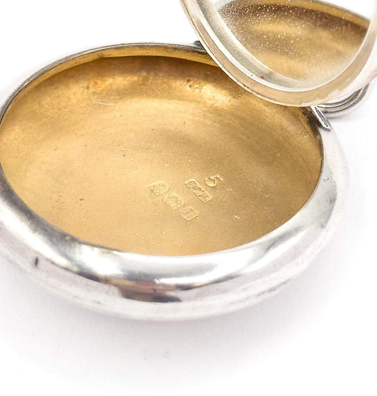 Close macro into the open base, where a row of small stamped hallmarks sits in the warm-toned interior, the hinged lid tilted up and out of focus above.