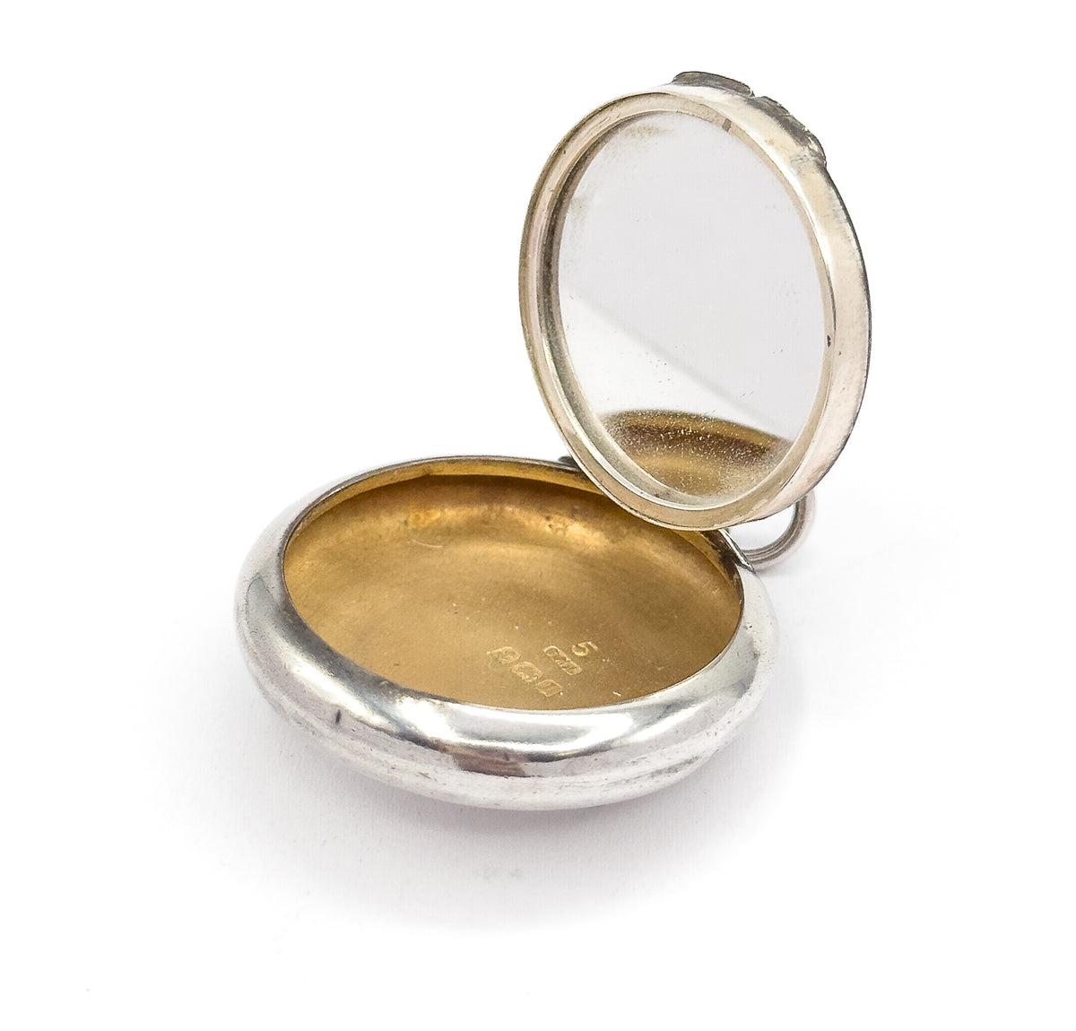 Angled from below, the locket stands open on its domed underside, showing the smooth outer curve of the base alongside the raised lid with its mirror and the small bail at the hinge.