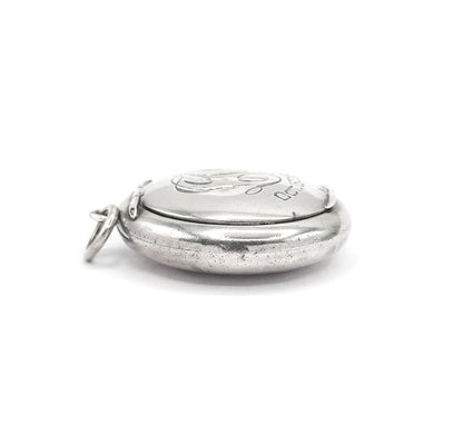 Edge-on side view of the closed locket, the domed base and lid meeting in a fine seam, the engraved front foreshortened and the bail ring projecting at the left.