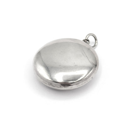 The closed locket seen from the back, its plain smooth dome filling the frame with no engraving on this face, the small bail ring set at the upper right.