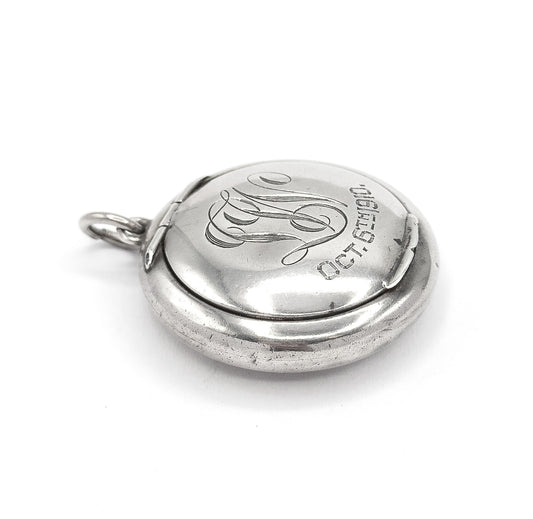 Tilted three-quarter view of the closed front, the flowing script initials and engraved date reading across the domed sterling silver lid, with the bail ring at the upper left.