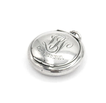 Angled from the opposite side, the engraved lid sits within the wider rim of the base, the seam running along the lower edge and the bail ring at the upper right, script initials and date upright.