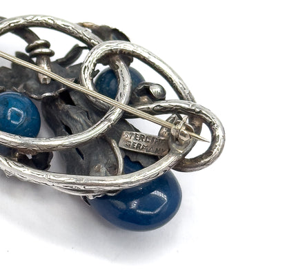 Close view of the back, where the later brooch pin stem crosses the openwork frame to its hook catch beside a plaque stamped Sterling Germany, with blue sodalite cabochons visible below.
