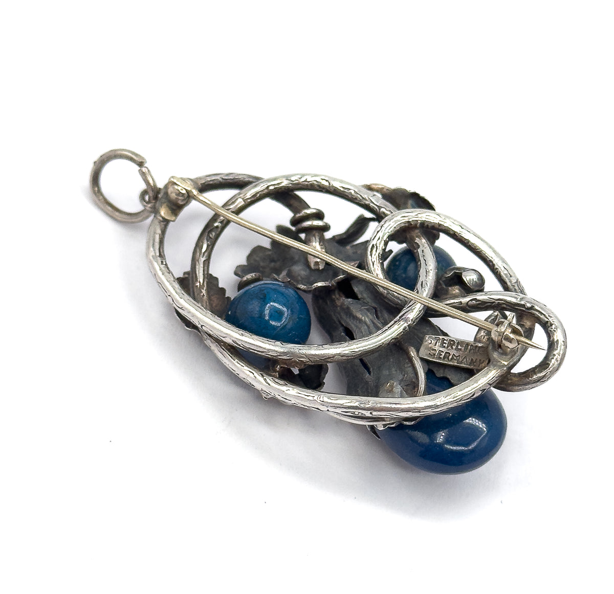 Almost the same view with slightly different angle, tilted so the round bail loop at the top and the full back of the openwork frame appear, with the pin stem running across to its catch.