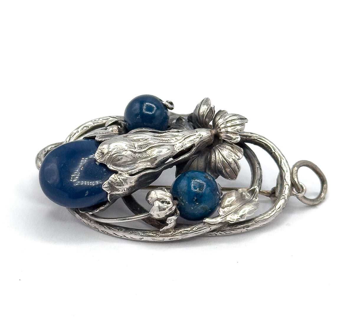Low side-on view of the front, showing the domed height of the large sodalite cabochon and two round beads among sculpted leaves, with the bail loop projecting at the right.