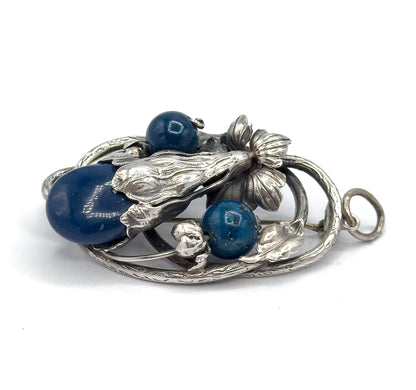 Low side-on view of the front, showing the domed height of the large sodalite cabochon and two round beads among sculpted leaves, with the bail loop projecting at the right.