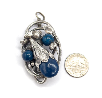 Front of the pendant laid beside a ten-cent coin for scale, the large oval sodalite cabochon and two round blue beads nestled in the leafy sterling silver frame below the bail loop.