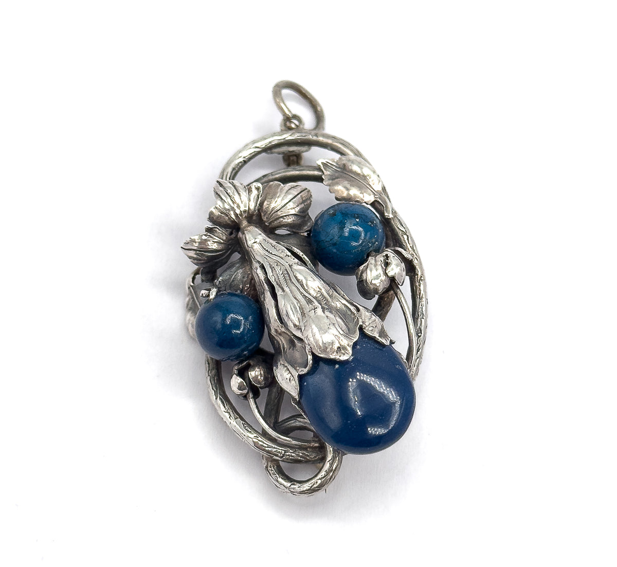 Upright front view against white, the whole oval openwork frame visible with its curling vine tendrils and small buds encircling the three deep blue stones beneath the bail loop.