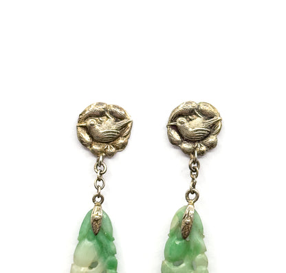 Cropped close on the upper halves alone, the two bird-motif tops side by side with their short chains and the pointed caps clasping the tips of the minty green carved jade, which runs out of frame.