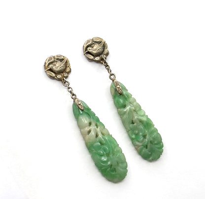 Closer overhead view with the pair fanning apart, the pierced flower carving on each minty green jade drop clearly readable and the chains curving from bird tops to pointed caps.