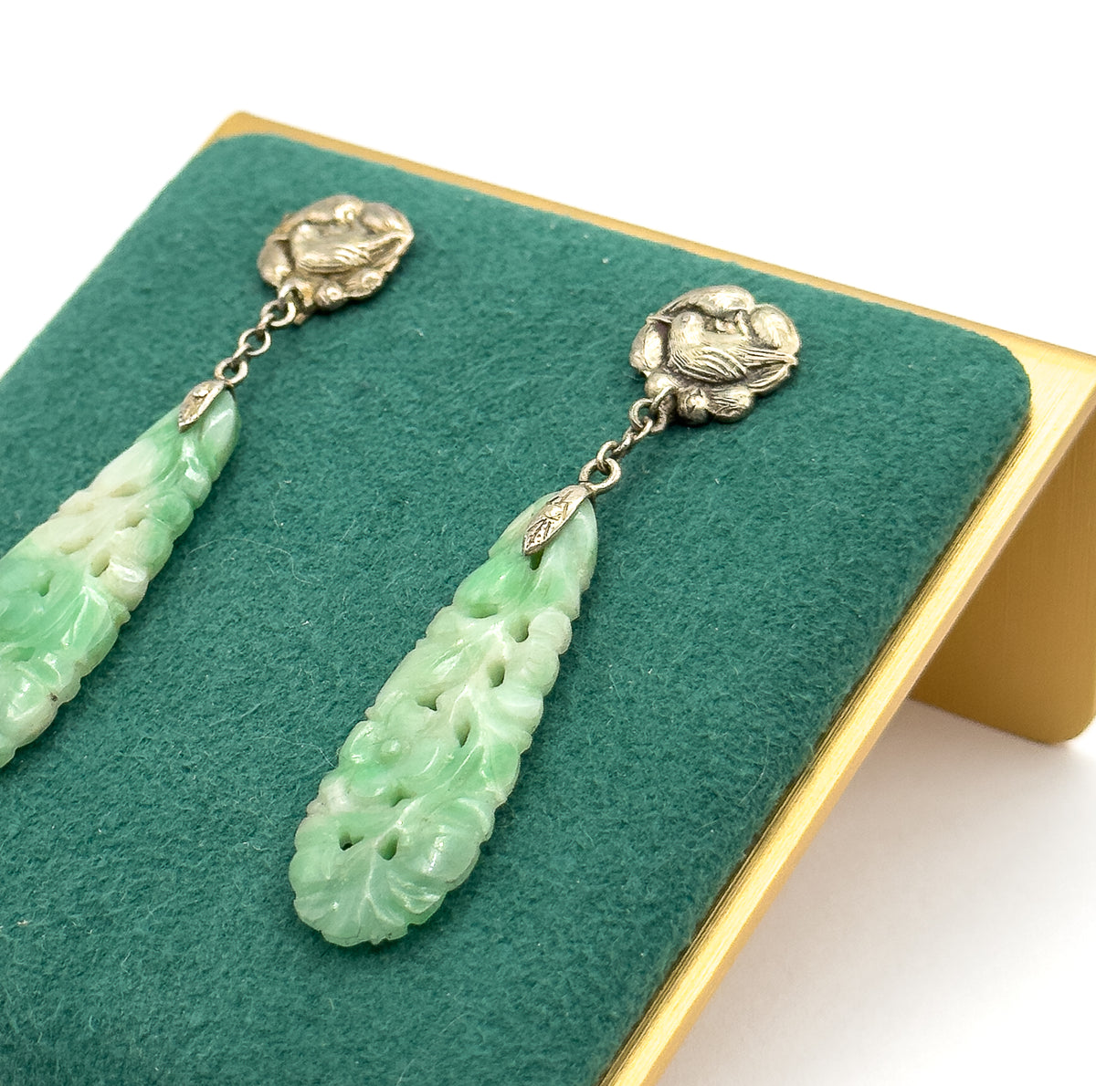 Angled close view on a green felt display stand, showing the embossed bird top, short chain link and pierced flower carving on each long minty green drop.