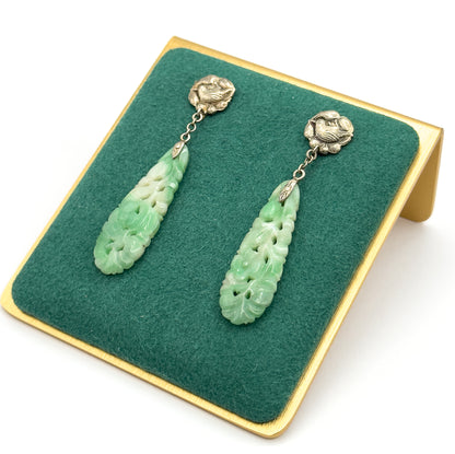 Overhead view of the pair laid side by side on the green felt of a gold-coloured stand, showing the full length from bird top and chain down to each pierced jade drop.