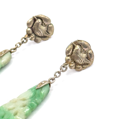 Tight front close-up of both embossed bird tops against white, the chain links running down to the pointed metal caps where each minty green carved jade drop begins at the lower edge.