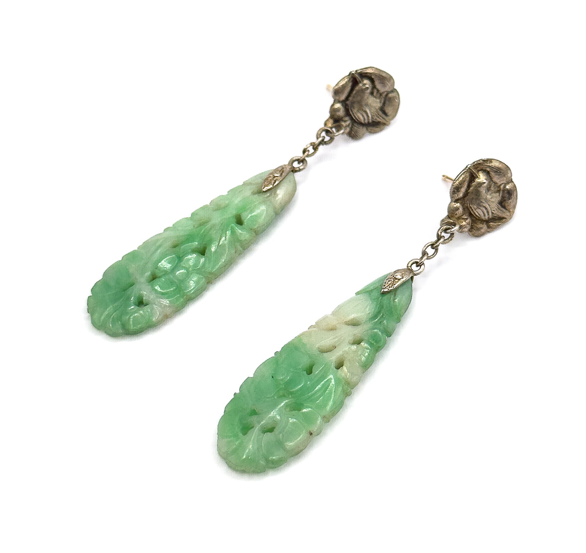 Angled full-length view of the pair on white, the two carved jade drops turned to show the flower carving across their broad faces below the chains and bird tops.
