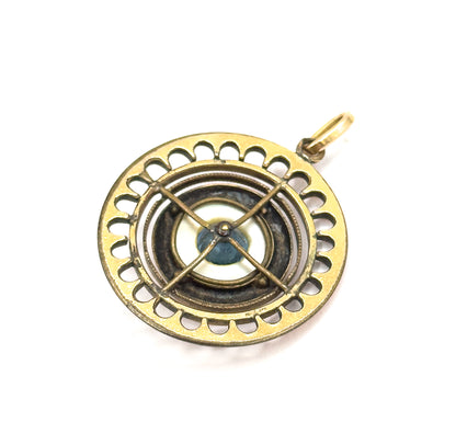 The reverse of the pendant, laid flat, showing the open scalloped rim, a crossed X-shaped support bar over the blue glass bead, and the small round bail at the top.