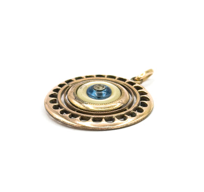 A low three-quarter angle showing the pendant's layered depth, with the mother of pearl ring stepping up to the domed blue glass bead and its small central paste stone.