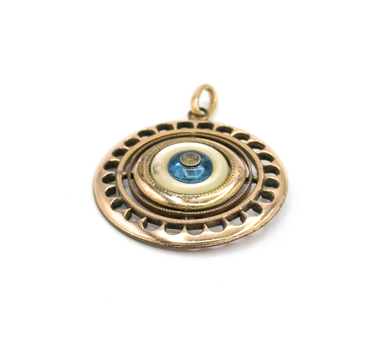 Tipped back with the bail standing upright at the top, the pendant seen slightly from the side so the scalloped rim curves away and the layered milgrain rings ring the blue glass bead.