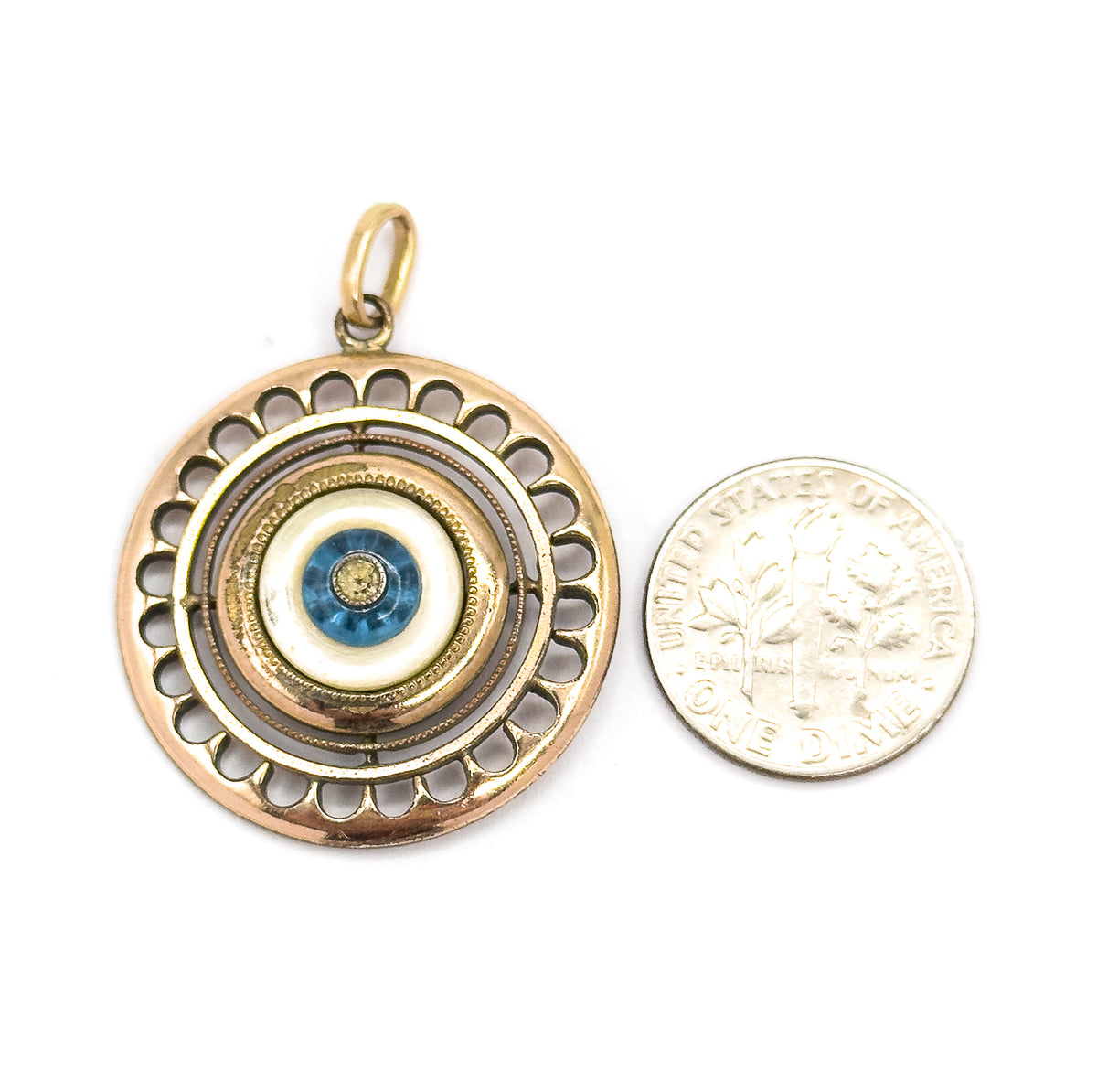 Shown face-up beside a ten-cent coin for scale, the pendant slightly larger than the coin, its scalloped rim, milgrain rings, mother of pearl and blue glass bead facing the viewer.