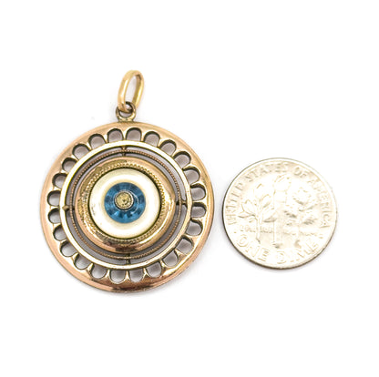 Shown face-up beside a ten-cent coin for scale, the pendant slightly larger than the coin, its scalloped rim, milgrain rings, mother of pearl and blue glass bead facing the viewer.