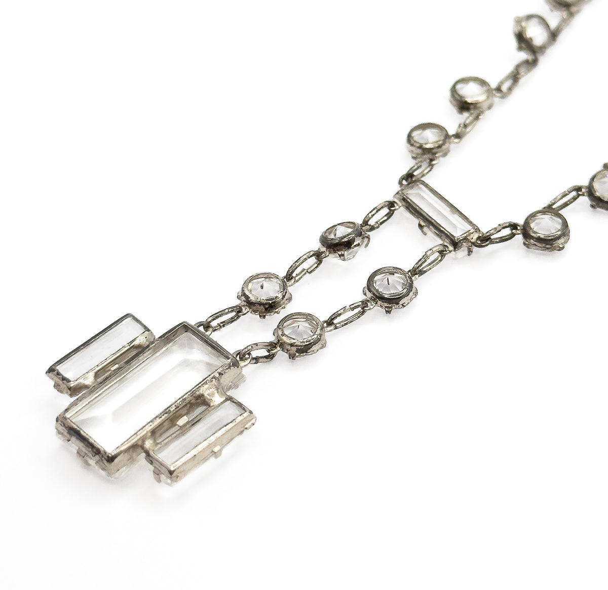 Close diagonal view along the chain, the round bezel-set stones and their linking loops running to the stepped rectangular drop at lower left, shown flat on white.