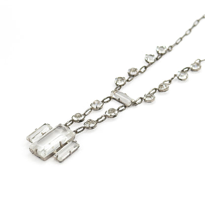 Raised three-quarter view in which the two chain strands split apart to carry the drop, letting the side walls of the settings and the stepped edges of the rectangular stones show against white.