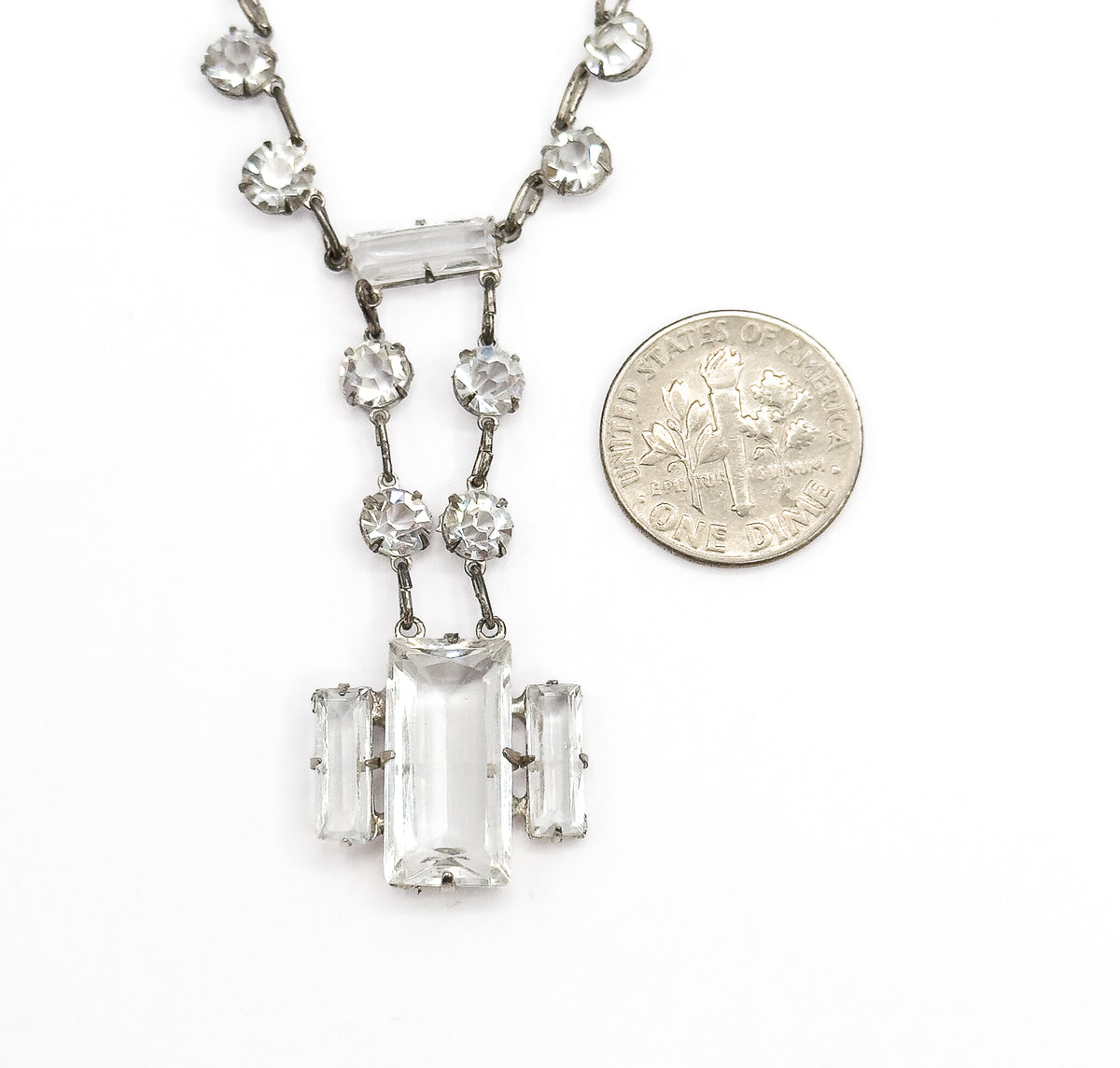 The drop laid flat beside a dime for scale, the coin roughly matching the height of the central rectangular stone and its two flanking bars.