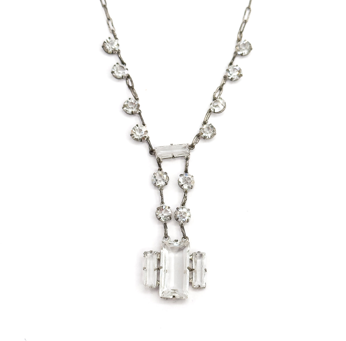 Straight-on full view of the whole necklace laid flat on white, round faceted stones spaced evenly down both sides of the chain to the symmetrical stepped rectangular drop at the centre.