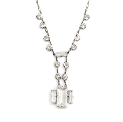 Straight-on full view of the whole necklace laid flat on white, round faceted stones spaced evenly down both sides of the chain to the symmetrical stepped rectangular drop at the centre.