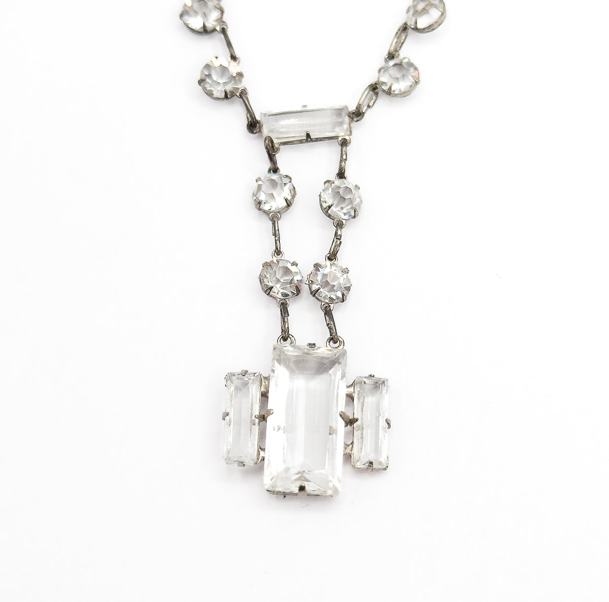 Tight close-up of the drop alone, the horizontal bar stone at its top, twin strands of round stones descending, and the central rectangular stone held by prongs between two upright bar stones.