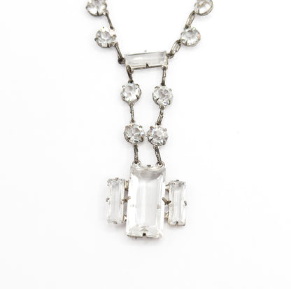 Tight close-up of the drop alone, the horizontal bar stone at its top, twin strands of round stones descending, and the central rectangular stone held by prongs between two upright bar stones.