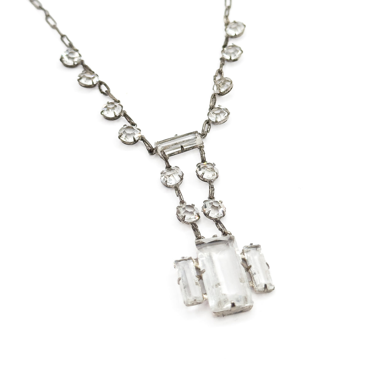 Diagonal view of the necklace's lower half, the two chain sides sweeping in from the top corners and the drop tilted toward the lower right, showing the small links joining each round setting.