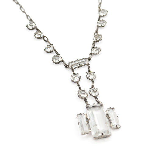 Diagonal view of the necklace's lower half, the two chain sides sweeping in from the top corners and the drop tilted toward the lower right, showing the small links joining each round setting.