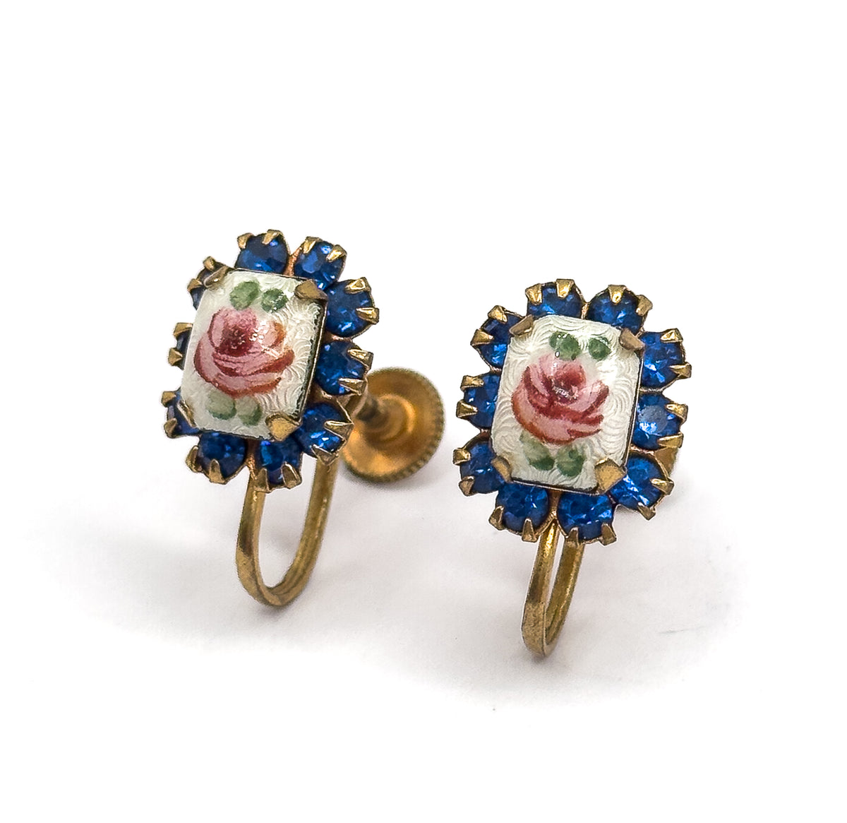 Close three-quarter view of the pair standing upright, the hand-painted enamel roses tilted toward the camera within their prong-set cobalt blue glass halos, curved screw wires below.
