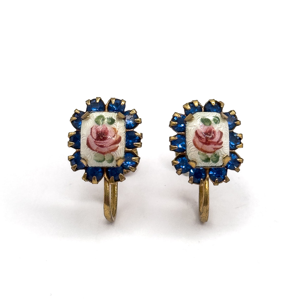 Straight-on front view of the pair side by side, each hand-painted enamel rose with green leaves centred in its prong-set cobalt blue glass halo, curved screw wires hanging below.