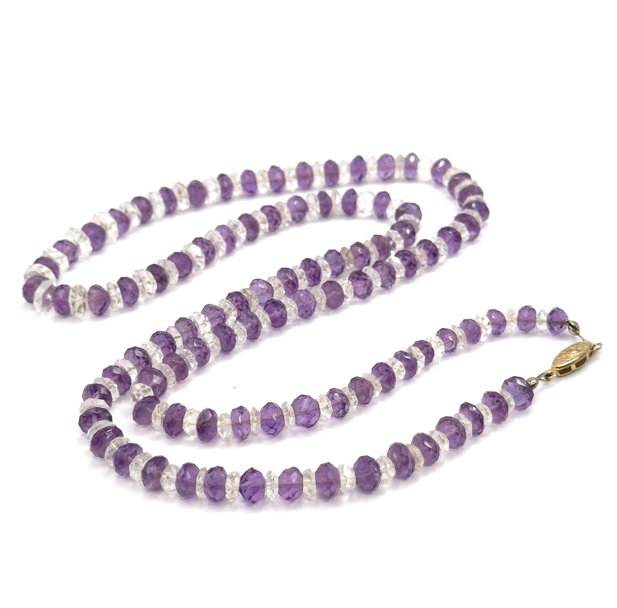 The whole necklace coiled in long loops on white, with the oval filigree base metal clasp lying at the right where the two ends of the graduated bead strand meet.