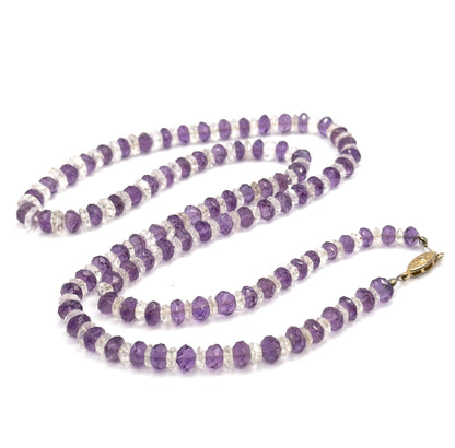 The whole necklace coiled in long loops on white, with the oval filigree base metal clasp lying at the right where the two ends of the graduated bead strand meet.