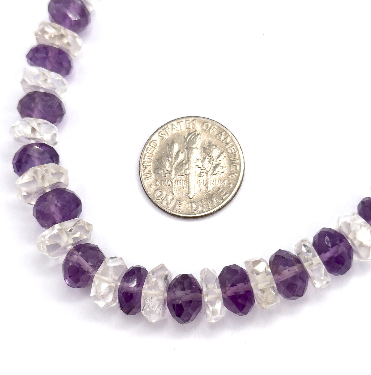 A curved section of the strand laid flat beside a dime, which shows the alternating amethyst and rock crystal rondelles to be roughly a quarter of the coin's width.