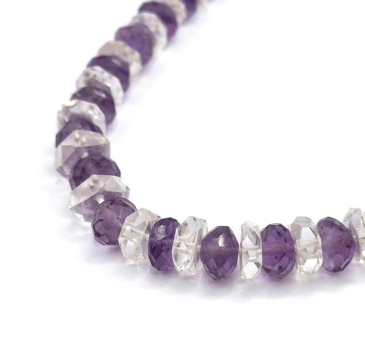 A close macro of one curve of the strand on white, the amethyst and rock crystal rondelles filling the frame so each faceted edge and the thread passing through them is visible.