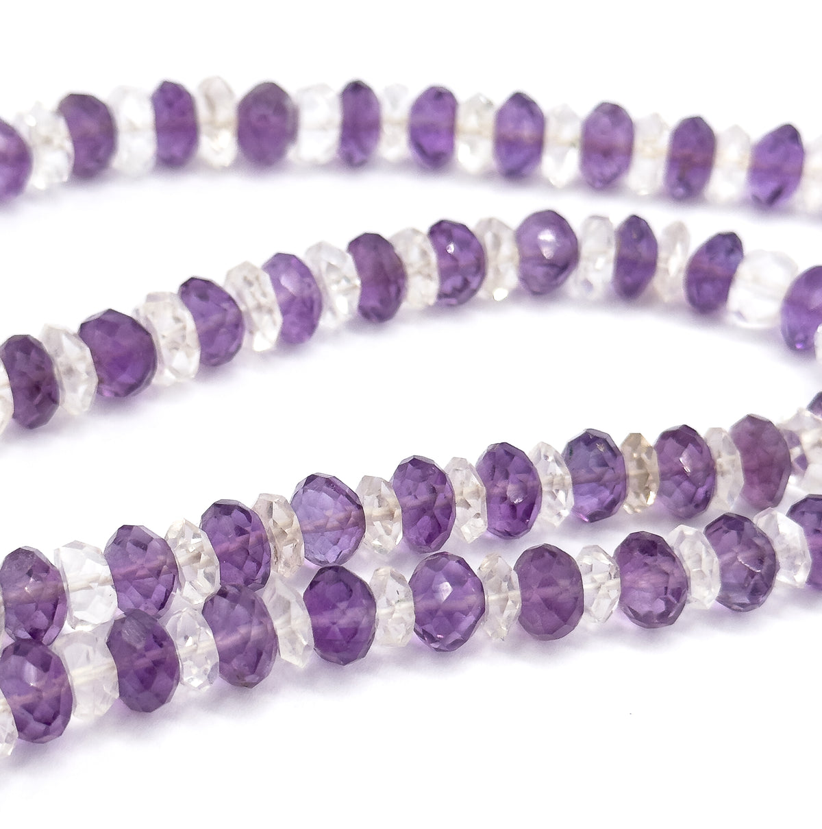 Three parallel rows of the looped strand fill the frame, showing how the clear rock crystal rondelles sit between each purple amethyst bead along the whole length.