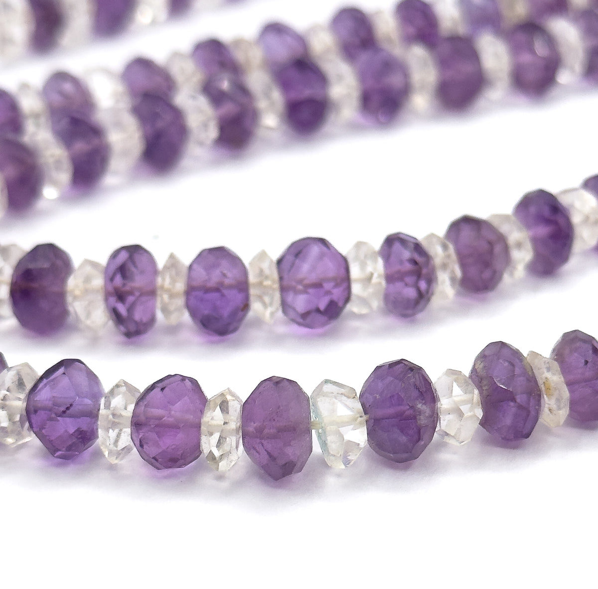 The lowest row is sharpest here, each amethyst rondelle showing its own depth of purple against the clear rock crystal spacers, while the rows above soften into blur.