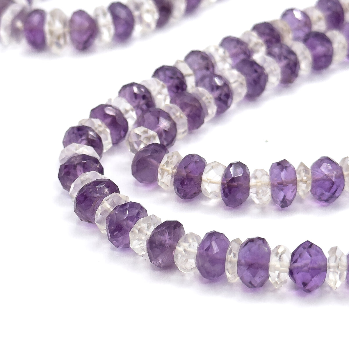 Tight macro from the side, where the flat faceted girdles of each amethyst and rock crystal rondelle meet face to face, with the strand's turn trailing off at the top corner.