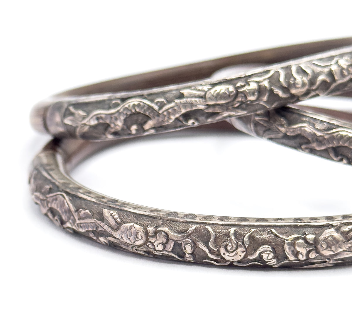 Looking down into the stack from above, the front bangle's inner curve fills the frame so the embossed scrollwork wraps over its rounded edge, with a wood section curving away at the upper left.