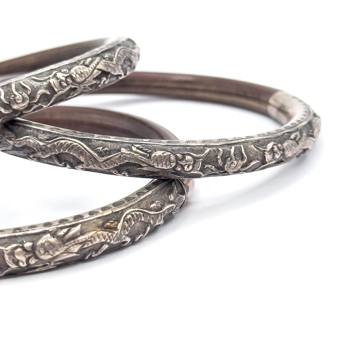 Angled close view from one side with the three bangles nested in overlapping ovals, the deep brown wood of the middle bangle sweeping right to meet its engraved silver join.