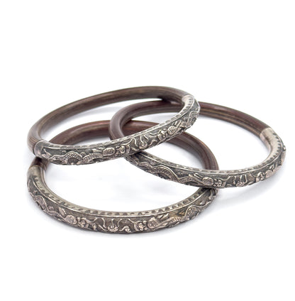 The three bangles overlap in a loose chain on white, each resting low so the long embossed silver fronts face the viewer together while the brown wood backs arc up behind.