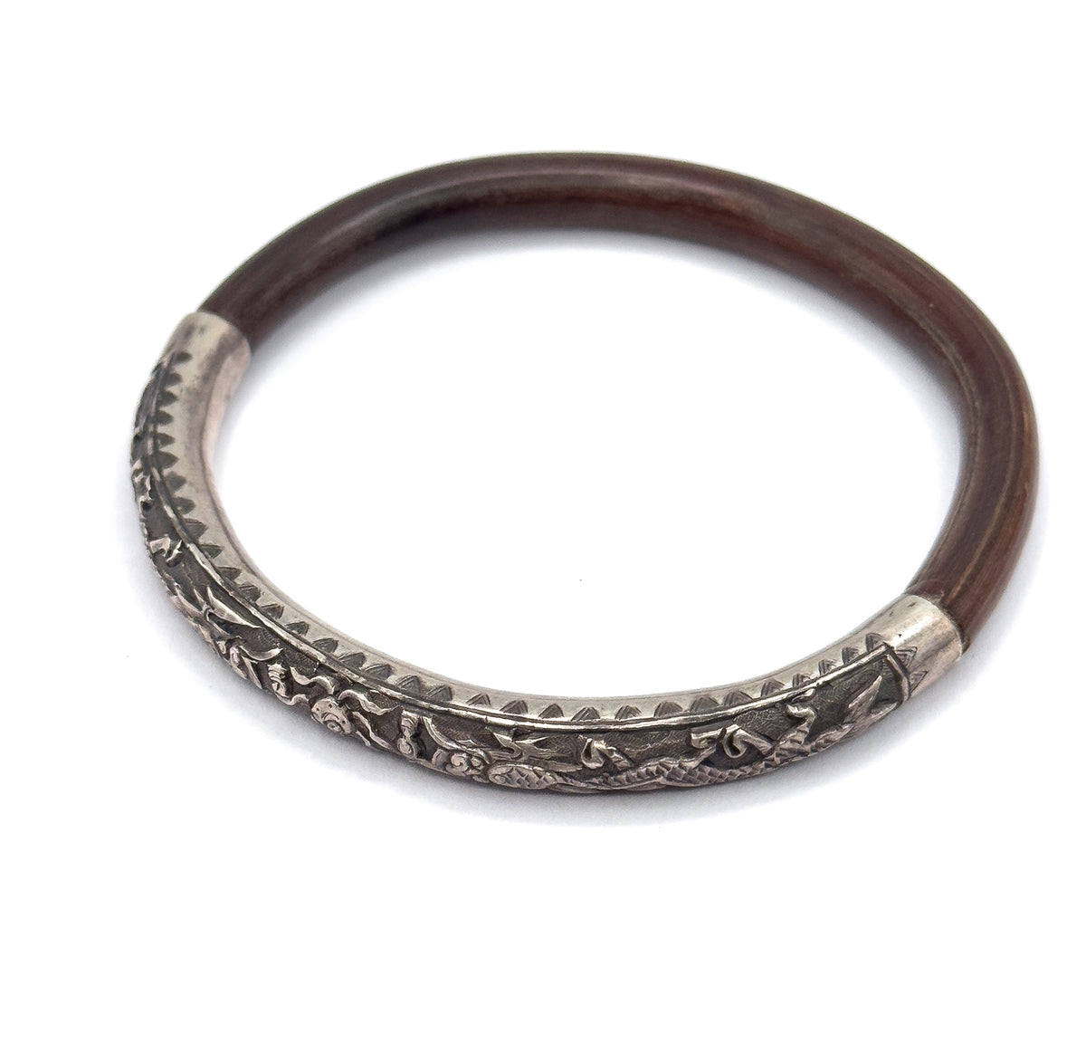 A single bangle lies flat on white, the deep brown wood band sweeping round to a sterling silver section embossed with raised figures and a toothed engraved border.
