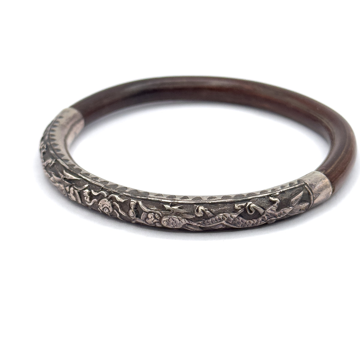 Tilted three-quarter view with the bangle standing on edge, bringing the silver section forward so its raised scaled figures, scrolling clouds and engraved border catch the light.