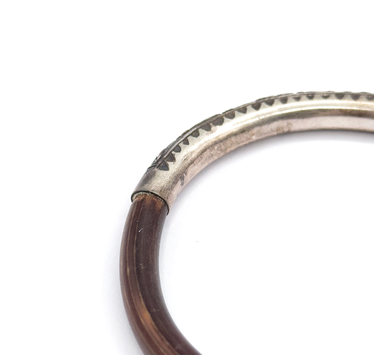 Close crop on one join, where the deep brown wood slips into the sterling silver section and the engraved row of triangular teeth runs along the band's upper edge.