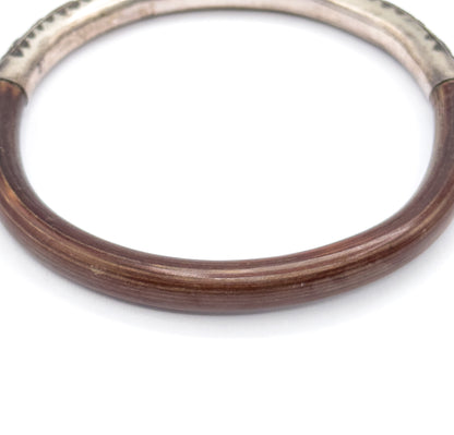 Close view of the lower half of the bangle, where the smooth deep brown wood shows fine lengthwise grain lines before rising to meet the silver section at both joins near the top.