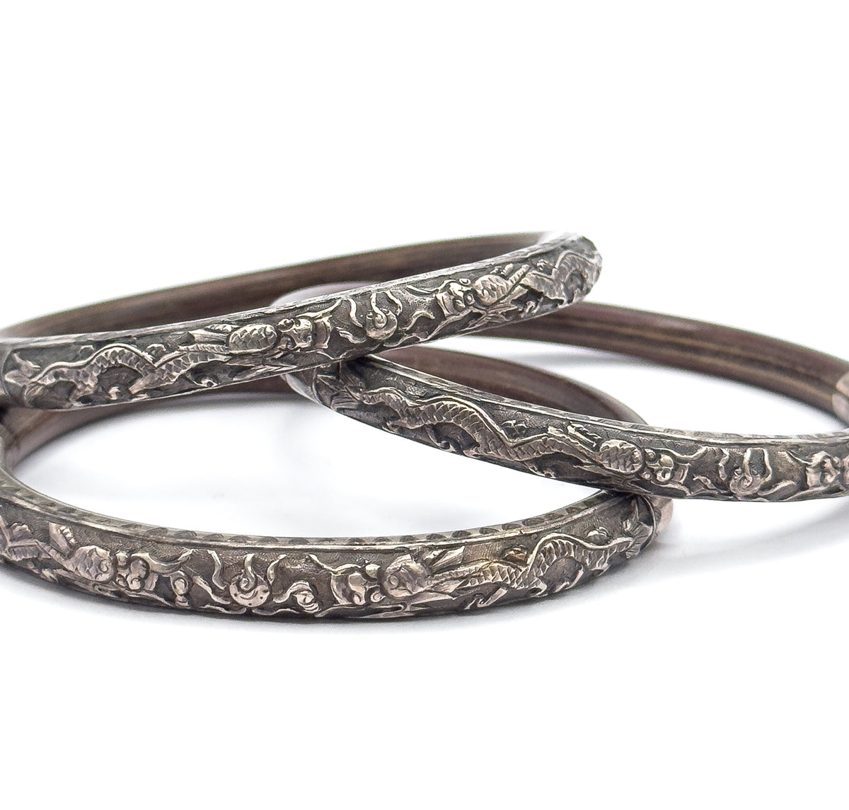 All three bangles stacked together on a plain white ground, their embossed silver sections aligned in overlapping arcs so the repeated engraved figures and clouds run across the set.