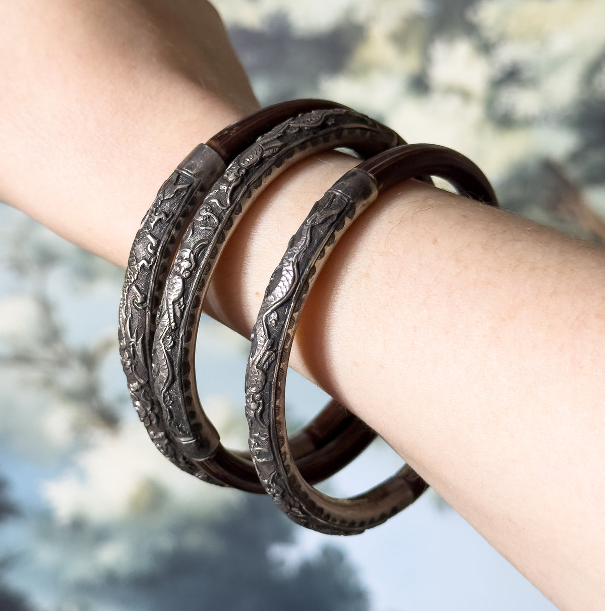 Set of three sterling silver and deep brown wood bangles, shown stacked on the wrist, with embossed and engraved patterned silver sections curving against the smooth polished wood.